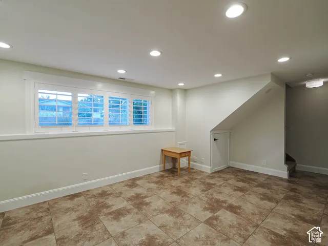Recessed lighting, tile flooring, window with shutters, under-stair storage, and a light-colored wall finish