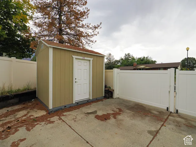 Outdoor storage shed with a panel door, accompanied by a white privacy fence and concrete paving