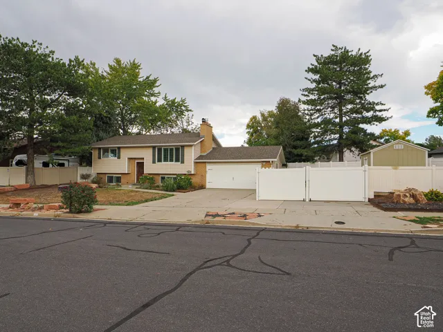 Split-level residence featuring a two-car garage, brick chimney, and mature trees
