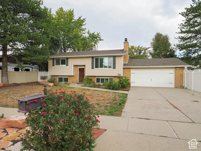 Split-level residence featuring a two-car garage, brick and siding exterior, established front landscaping, and a concrete driveway