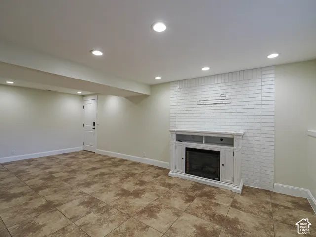 Recessed lighting throughout, tile flooring, white brick-patterned accent wall, and a built-in fireplace with white mantel and surround