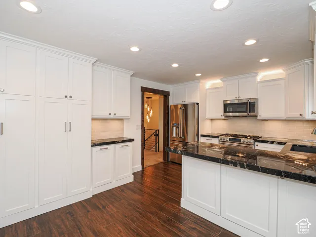 White shaker cabinetry, black granite countertops, stainless steel appliances, wood-finish flooring, and recessed ceiling lighting