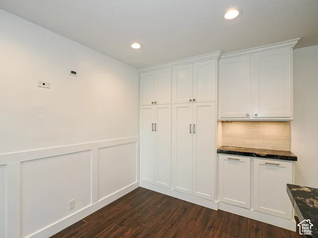 White shaker cabinetry with crown molding, dark wood-finish flooring, wainscoting, black textured countertops, and a subway tile backsplash