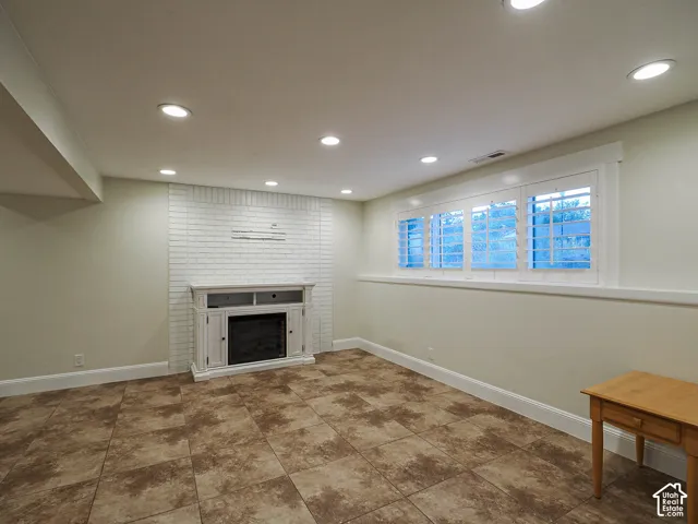 Tile flooring, white brick-finish accent wall, built-in electric fireplace, recessed lighting, and plantation shutters