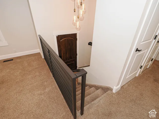 Staircase featuring dark metal railing, carpeted treads, and a multi-bulb pendant light fixture