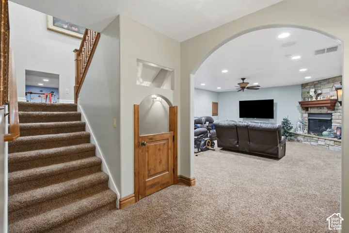 Carpeted staircase with wood railing, arched doorway, and stone fireplace with wood mantel