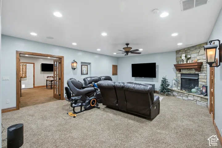 Spacious recreation room featuring recessed ceiling lighting, ceiling fan, stone fireplace with built-in shelving, wall-mounted flat-screen television, and neutral carpet flooring throughout