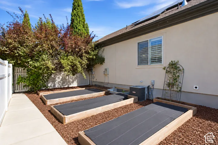 Exterior featuring a stucco finish, multiple raised garden beds, a concrete pathway, a white privacy fence, and mature trees