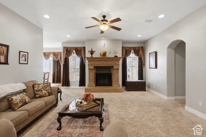 Spacious living area featuring a central fireplace with an ornate mantel, plush carpet, recessed lighting, and a ceiling fan