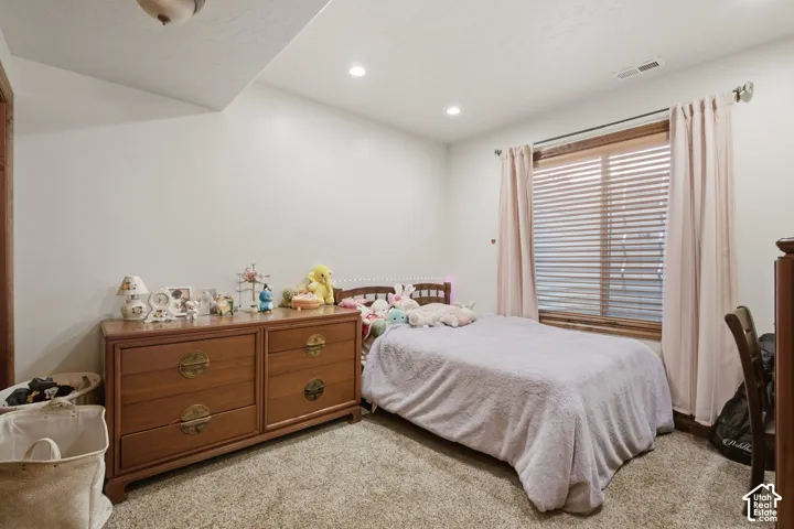 Comfortable bedroom featuring carpeted flooring, wood-finish dresser with brass hardware, and large sliding glass doors with shutters and sheer curtains allowing natural light throughout the space