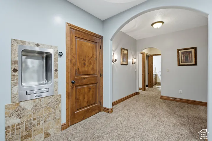 Built-in stainless steel drinking fountain with tile surround, wood-paneled door, and archway with recessed lighting