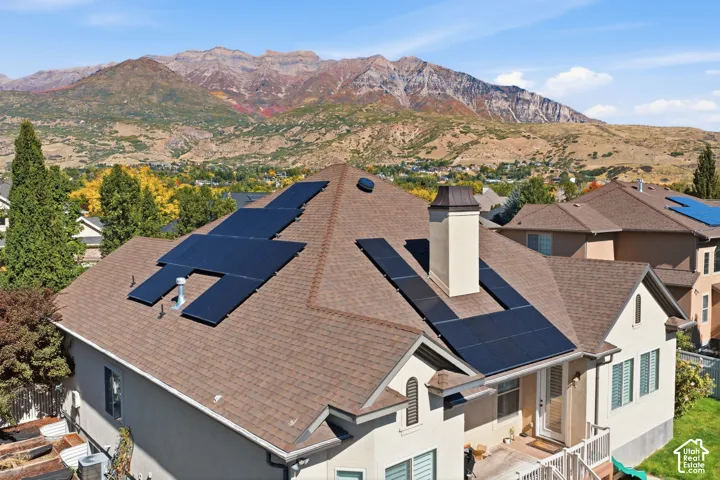 Shingle roof with integrated solar panels, stucco exterior, and a prominent chimney with a metal cap