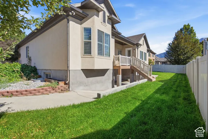 Stucco exterior with a bay window, composite deck with wood railings, concrete patio, and a manicured lawn enclosed by a privacy fence