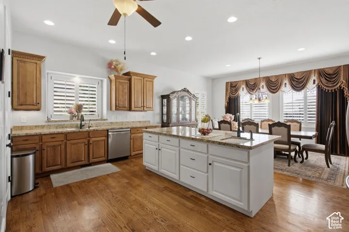 Wood-finish flooring throughout, kitchen island with built-in sink, recessed lighting, wood-finish cabinetry, and stainless steel dishwasher