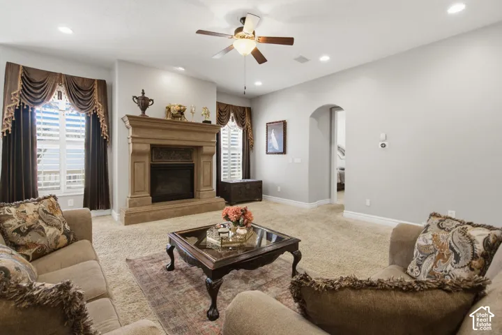 Central fireplace with a detailed mantel, recessed lighting, ceiling fan, arched doorway, and carpeted flooring