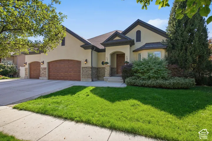 Stunning stucco and stone exterior featuring a welcoming arched entryway, dual brick-finish garage doors, and distinctive peaked roofline with dark architectural accents