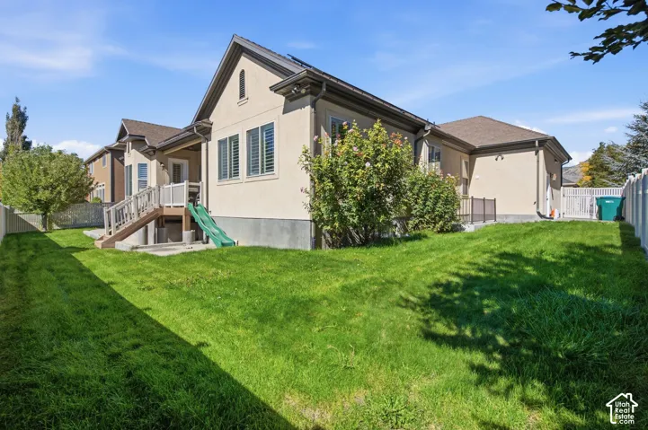 Expansive green lawn with mature landscaping, partial fencing, and a rear deck with staircase