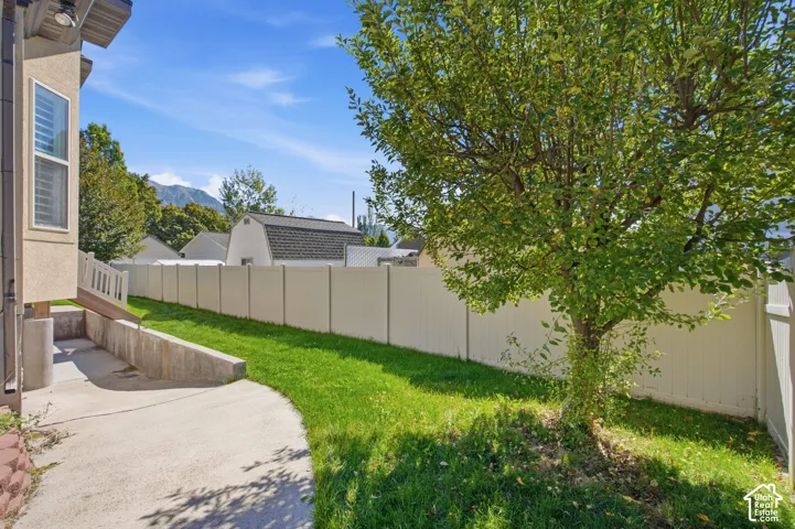 Private yard with a mature tree, concrete pathway, and durable vinyl fencing