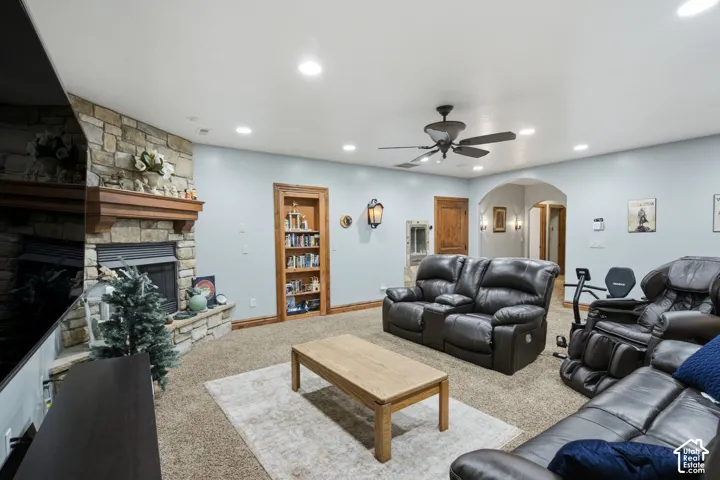 Stone fireplace with wood mantel, recessed lighting, ceiling fan, built-in shelving, and arched hallway entry