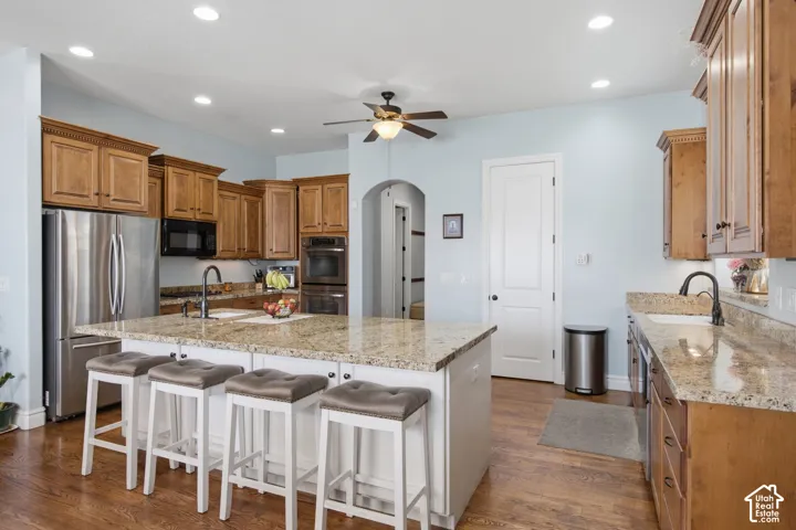 Kitchen featuring a large island with a stone countertop, wood-finish flooring, recessed lighting, ceiling fan, and stainless steel appliances