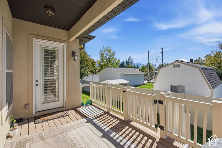 Covered patio featuring wood-finish decking, a white railing, and an exterior wall light fixture