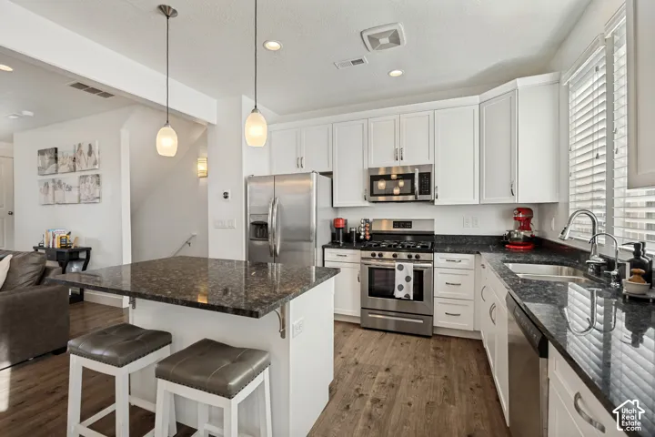 Kitchen featuring stainless steel appliances, white cabinetry, dark stone countertops, wood-finish flooring, and a kitchen island with pendant lighting
