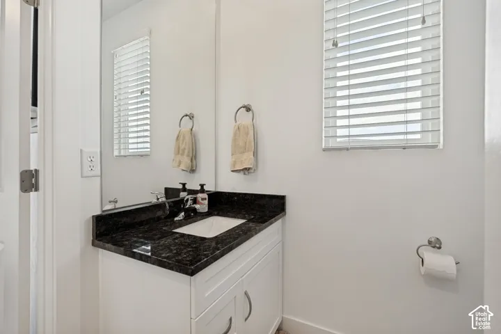 White vanity with shaker-style cabinetry, a dark countertop, and an undermount sink