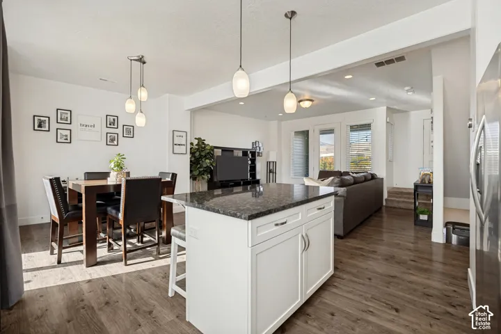 Kitchen island with granite countertop, wood-finish flooring, recessed lighting, and pendant light fixtures