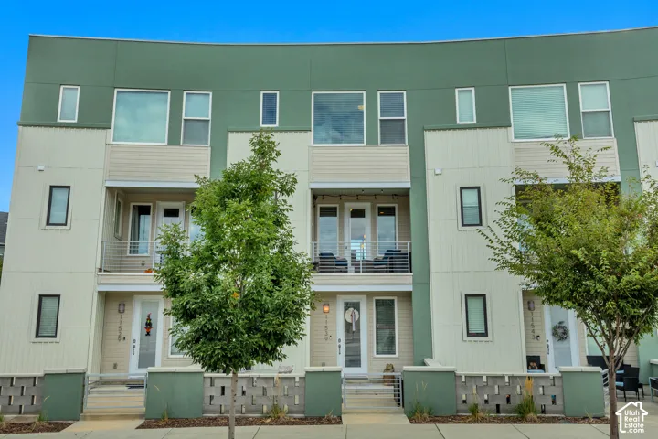Modern facade with a flat roofline, multiple balconies featuring metal railings, and a mix of panel and horizontal siding