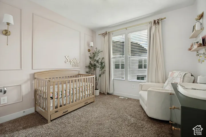 Wall paneling with decorative molding, dual wall sconces, large windows with blinds, and neutral tone carpeting