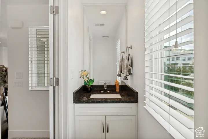 White vanity with cabinet storage, dark stone countertop, integrated rectangular sink, and a large wall-mounted mirror