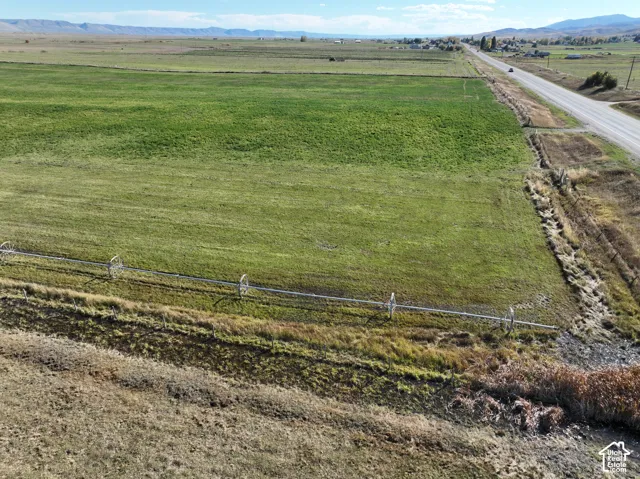 Expansive green field featuring a visible irrigation system, a paved road, and distant mountains
