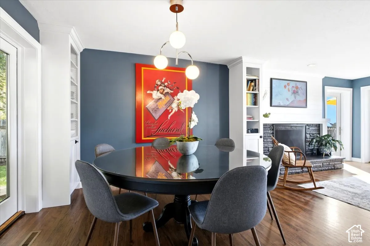 Hardwood flooring, custom built-in cabinetry, fireplace with stone surround, and a modern ceiling light fixture