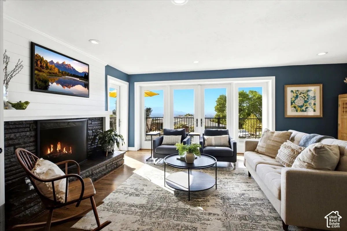Fireplace with a stone surround and mantel, wood-finish flooring, recessed lighting, and multiple paneled glass doors leading to an exterior balcony
