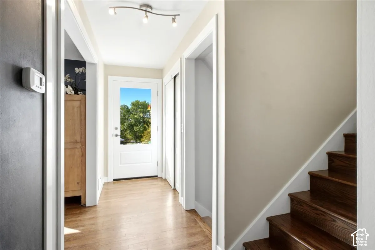 Hardwood flooring, white paneled door with glass insert, track lighting fixture, and hardwood stairs with white risers