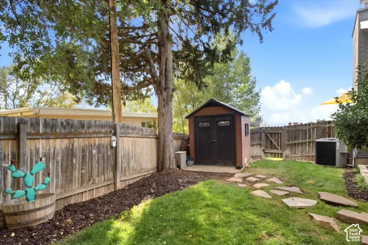 Backyard featuring a wooden privacy fence, mature trees, a storage shed, and flagstone pavers