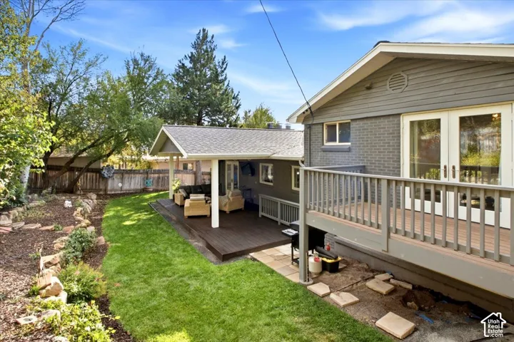 Expansive backyard featuring a manicured lawn, a raised wood-finish deck with railings, and a covered patio with a shingle roof