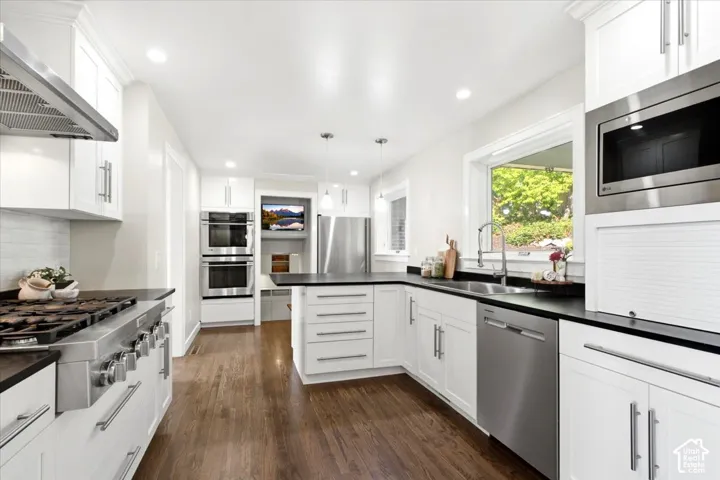 White cabinetry, dark countertops, stainless steel appliances, wood-finish flooring, and recessed lighting