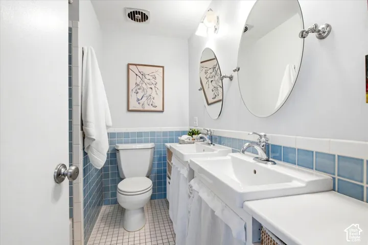Dual pedestal sinks with chrome fixtures, oval mirrors, white tile flooring, and blue square wall tiling