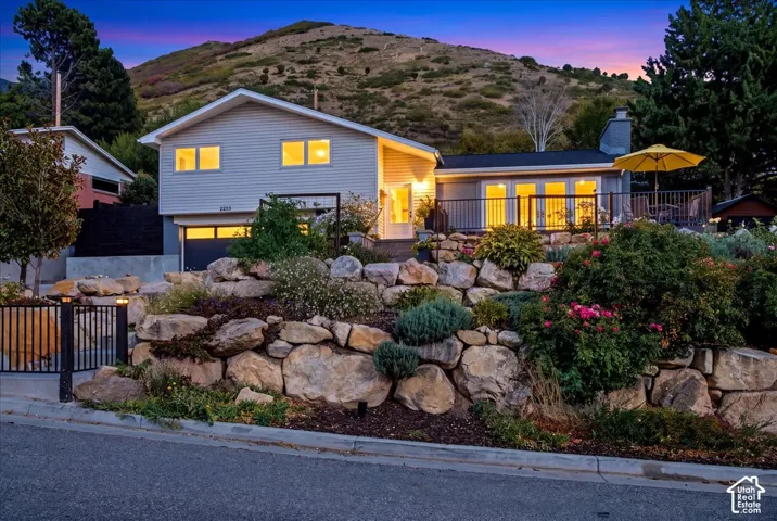 Split-level exterior with light siding, a spacious deck, and a prominent retaining wall with integrated landscaping