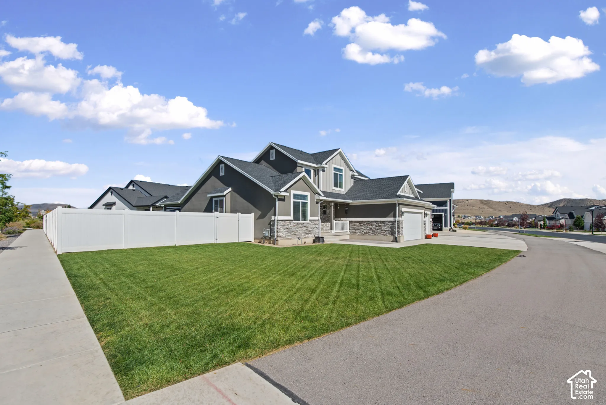 Contemporary exterior with a two-car garage, stone and siding accents, a manicured lawn, and a white privacy fence