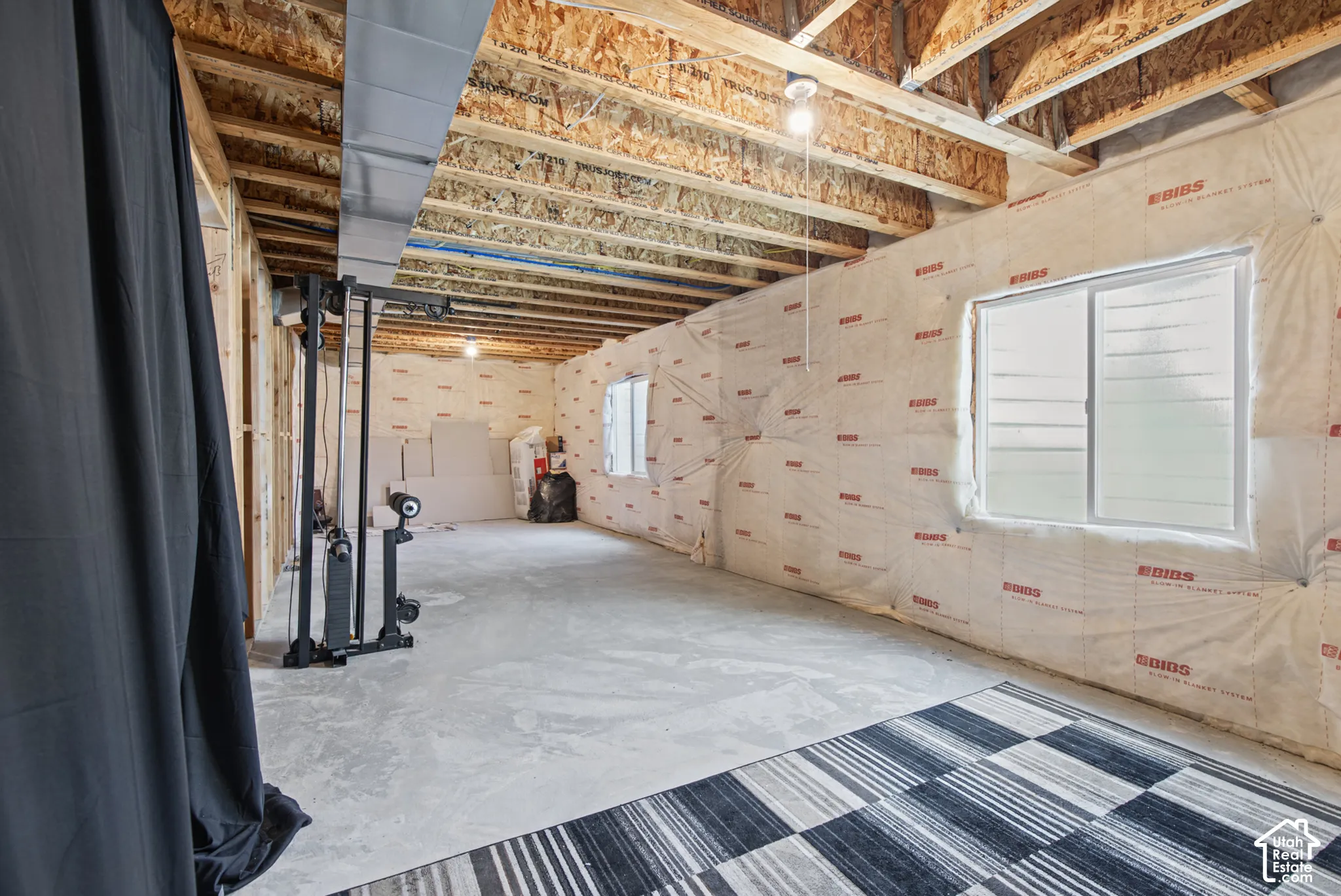 Unfinished basement with exposed ceiling joists, framed walls, visible insulation, and two windows