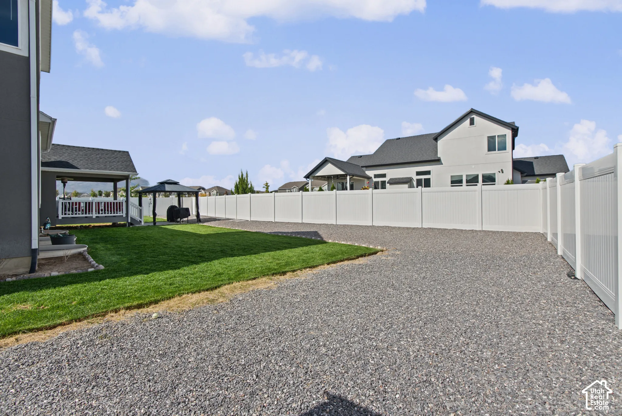 Expansive gravel surface, manicured lawn, white privacy fencing, and covered patio