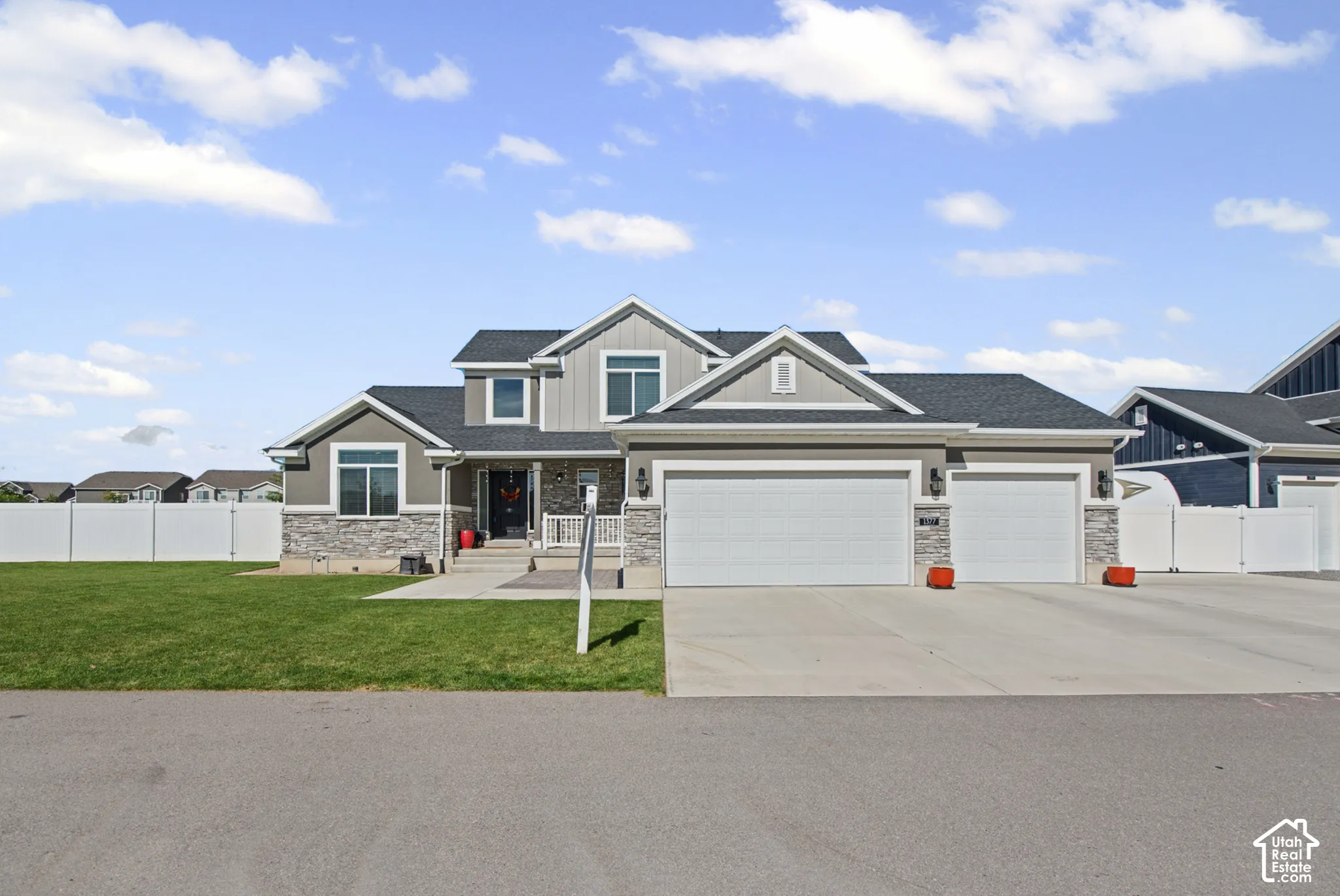 Two-story exterior with a stone and siding facade, featuring a dual-bay garage with individual doors, a covered entry, and a front lawn with a white vinyl fence