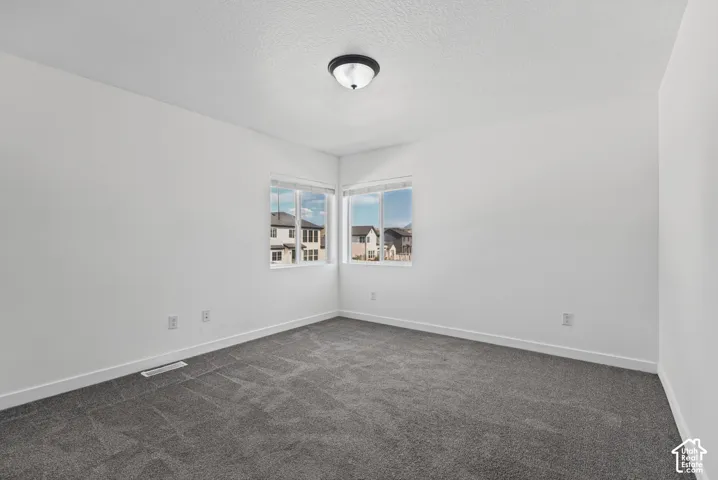 Neutral wall paint with textured finish, corner window placement, and dark gray carpet flooring
