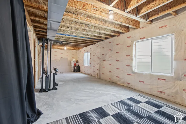Unfinished basement with exposed ceiling joists, framed walls, visible insulation, and two windows