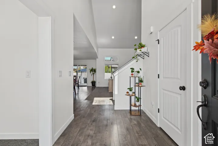 Vaulted ceiling, recessed lighting, wood-finish flooring, white paneled door, and a staircase