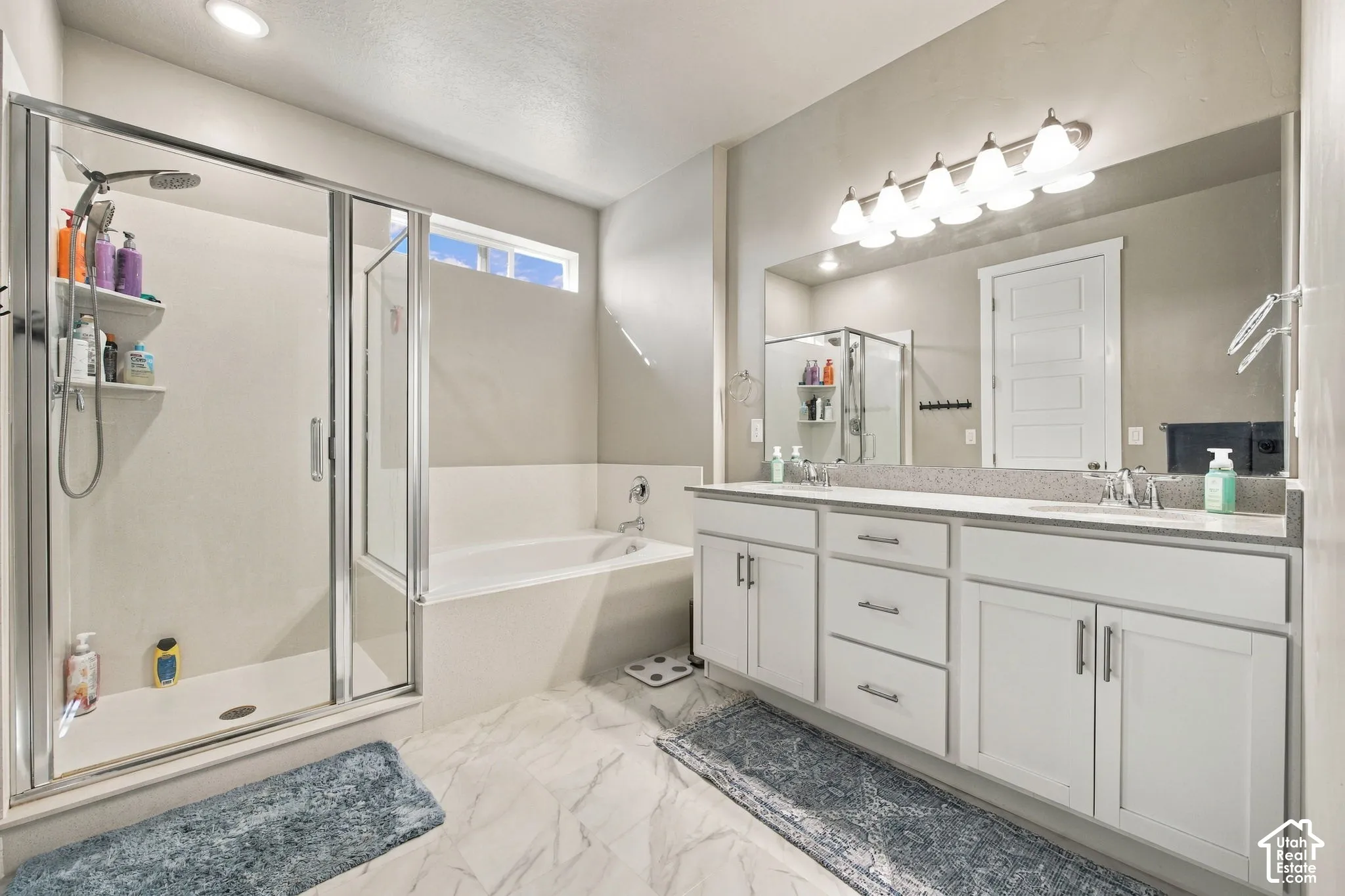 Primary - Dual vanity with white cabinetry and chrome hardware, a built-in bathtub, a glass-enclosed shower, and a high transom window