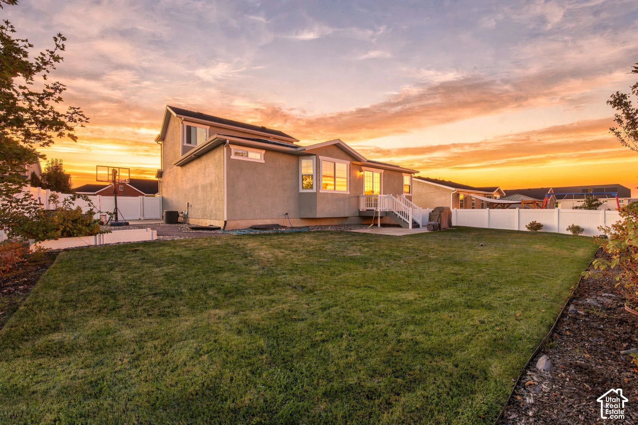 Expansive green lawn, stucco exterior, white privacy fencing, elevated rear deck, and a concrete patio