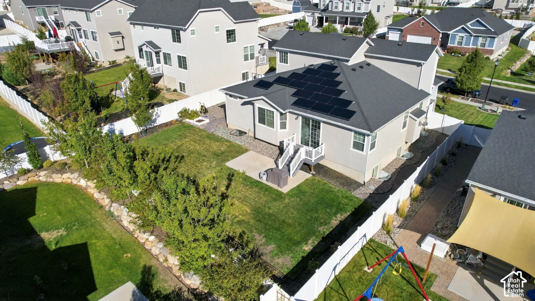 Rear exterior featuring a spacious lawn, integrated solar panels, a private patio, and a white vinyl fence